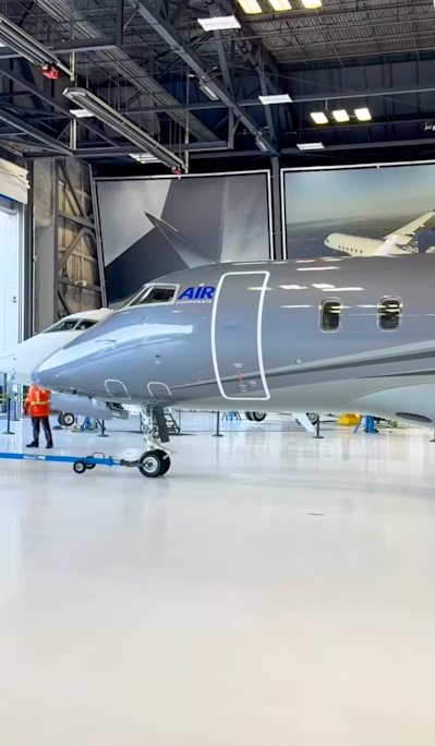 Gray business jet photographed beneath mixed overhead hangar lighting