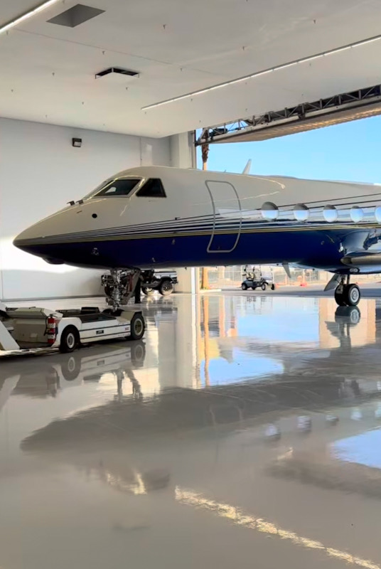Blue and white business jet at a hangar threshold with a natural reflection on the polished floor