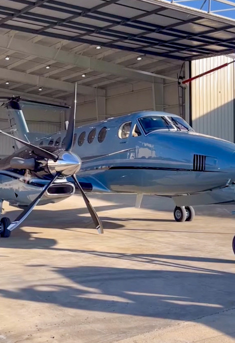 Silver blue turboprop aircraft in strong sunlight at a hangar opening