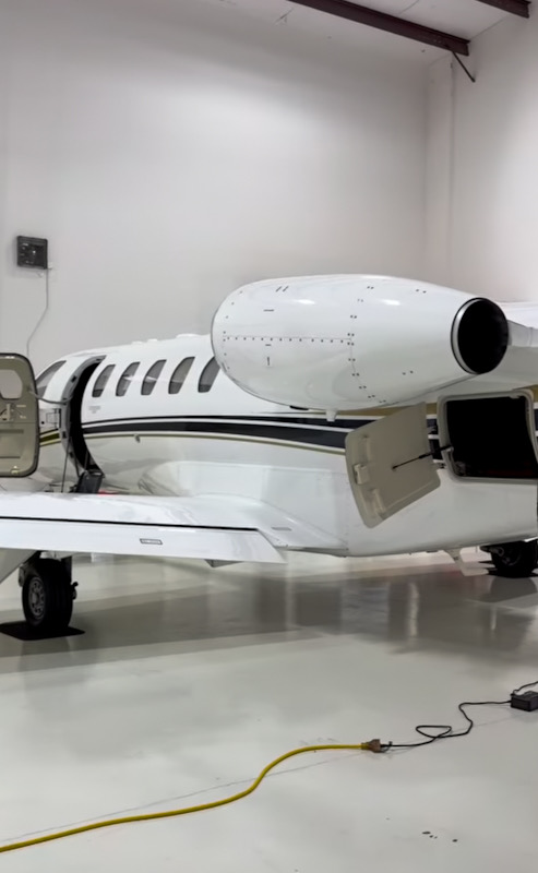 Rear engine and open service panels on a white business jet inside a hangar